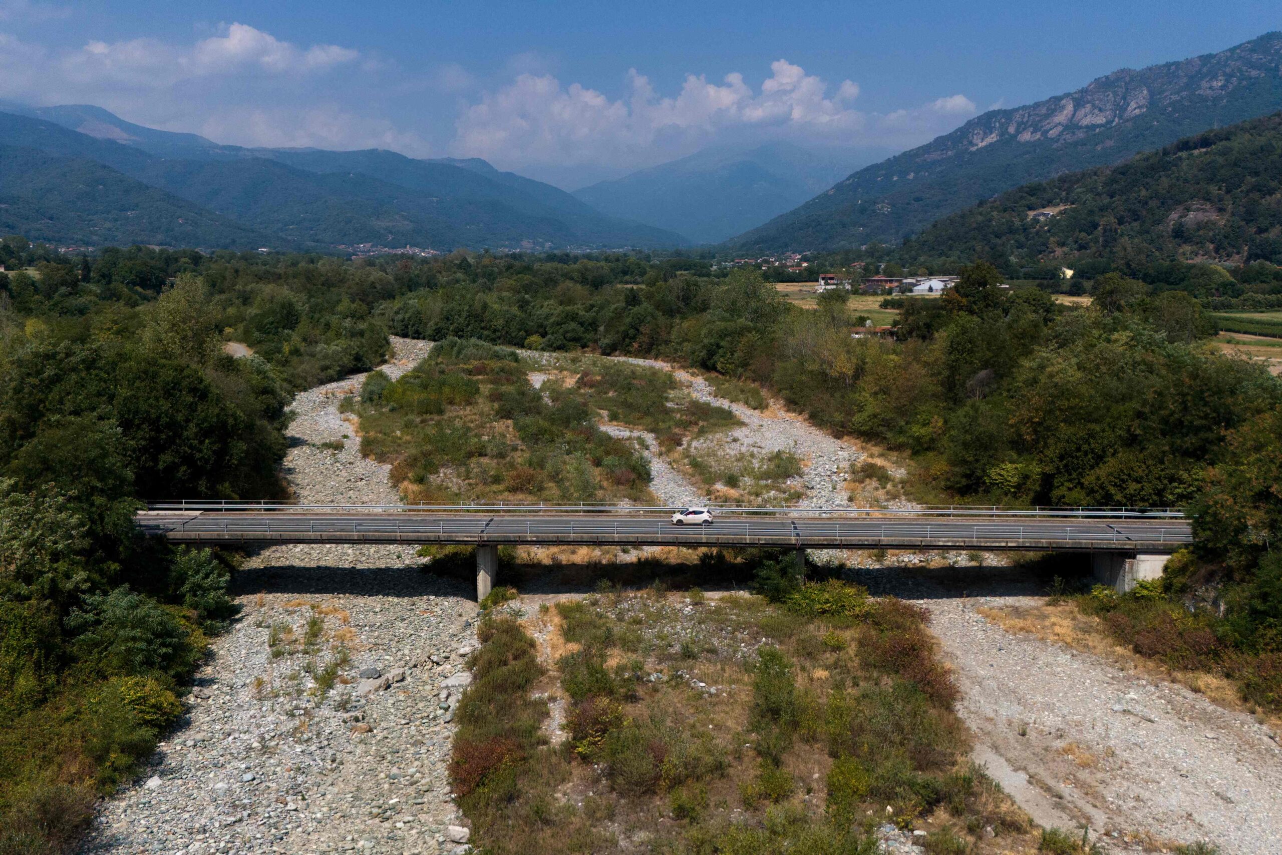 TOPSHOT - This aerial view shows a car crossing the bridge over the Po River in Martiniana Po, on July 30, 2026. The Po Valley in northern Italy is facing a severe water and drought crisis driven by intense summer heatwaves and sparse rainfall. Water levels and river flow have plummeted rapidly, exposing sandbanks and triggering urgent concerns for regional agriculture and ecosystems. (Photo by Marco Bertorello / AFP)